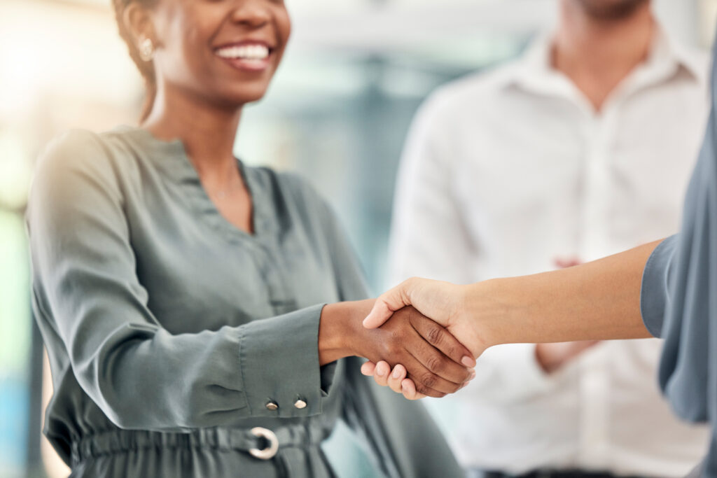Two interracial professionals shaking hands in an office setting.